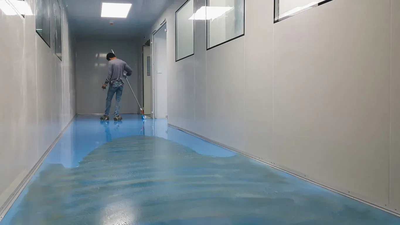 Person mopping a glossy blue hallway floor in a narrow corridor with beige walls.