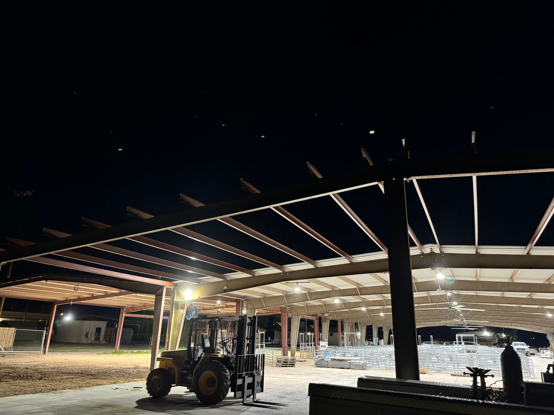 A forklift is parked under a covered area at night.