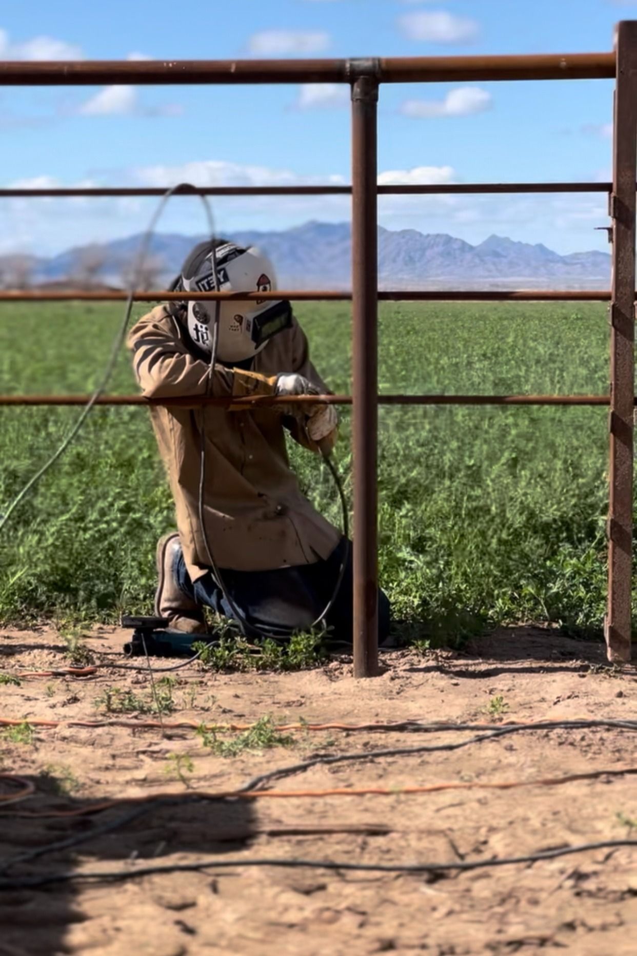 A man is welding a fence in a field.