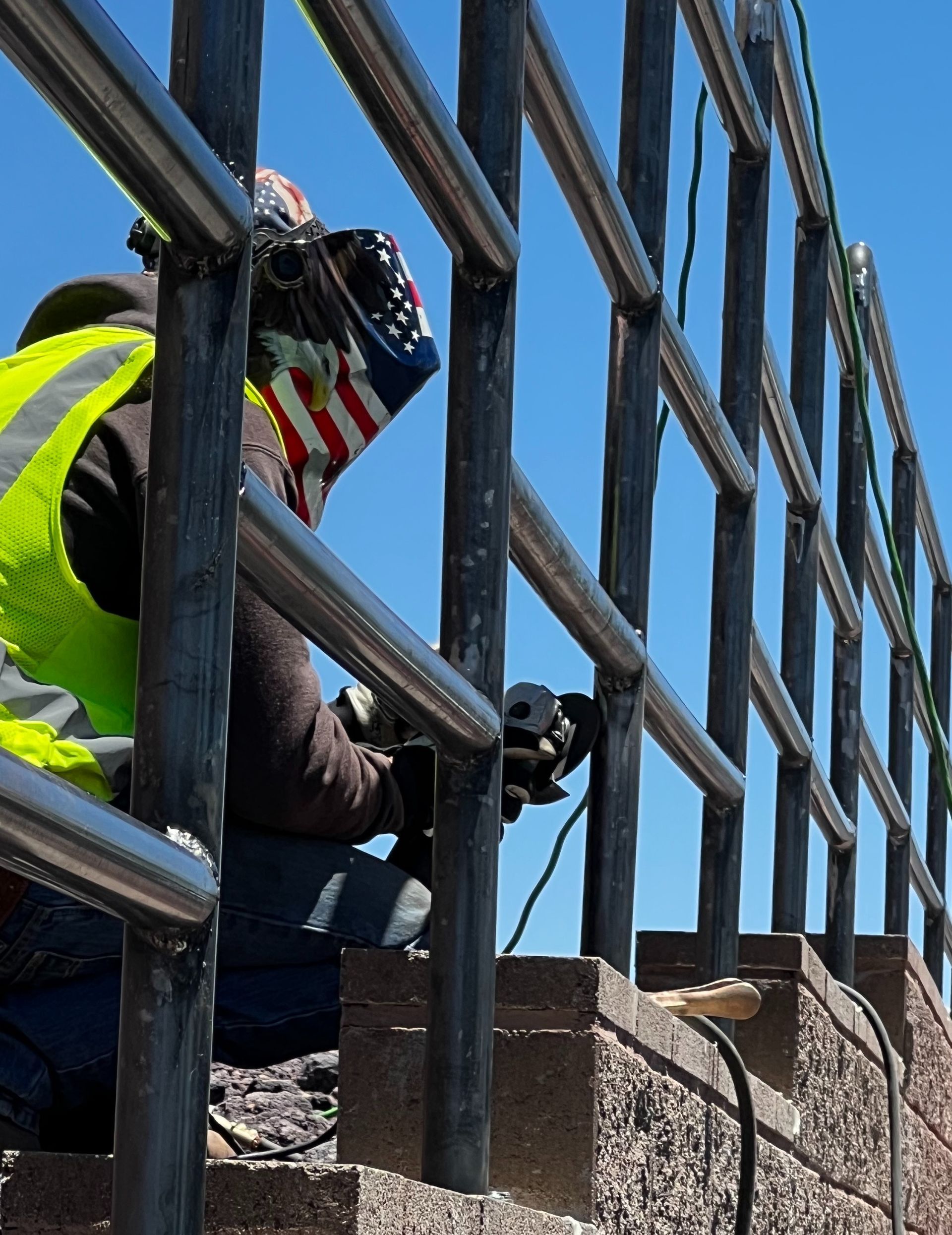 A man wearing a welding mask is working on a fence