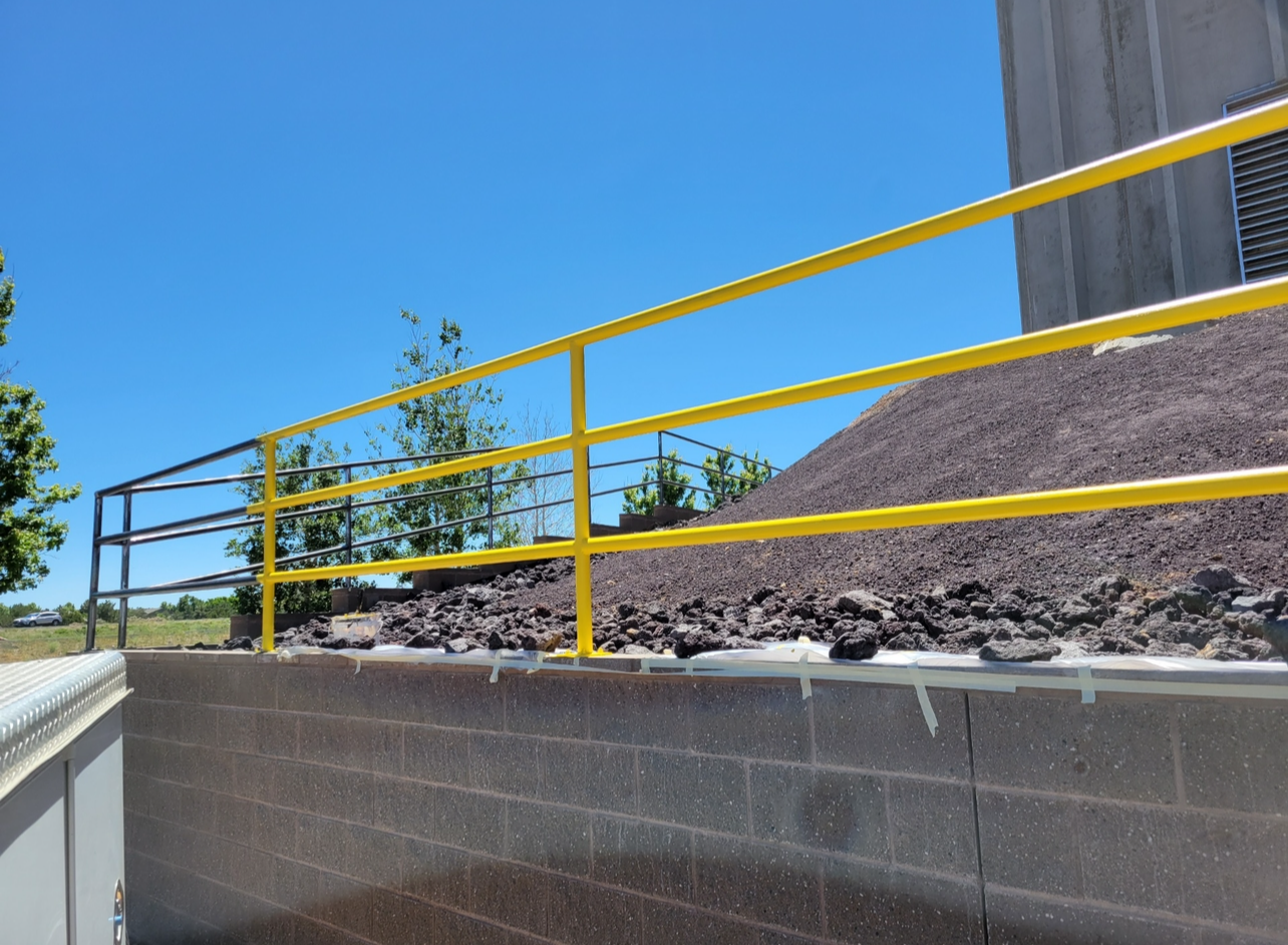 A yellow railing on a brick wall with a pile of rocks in the background