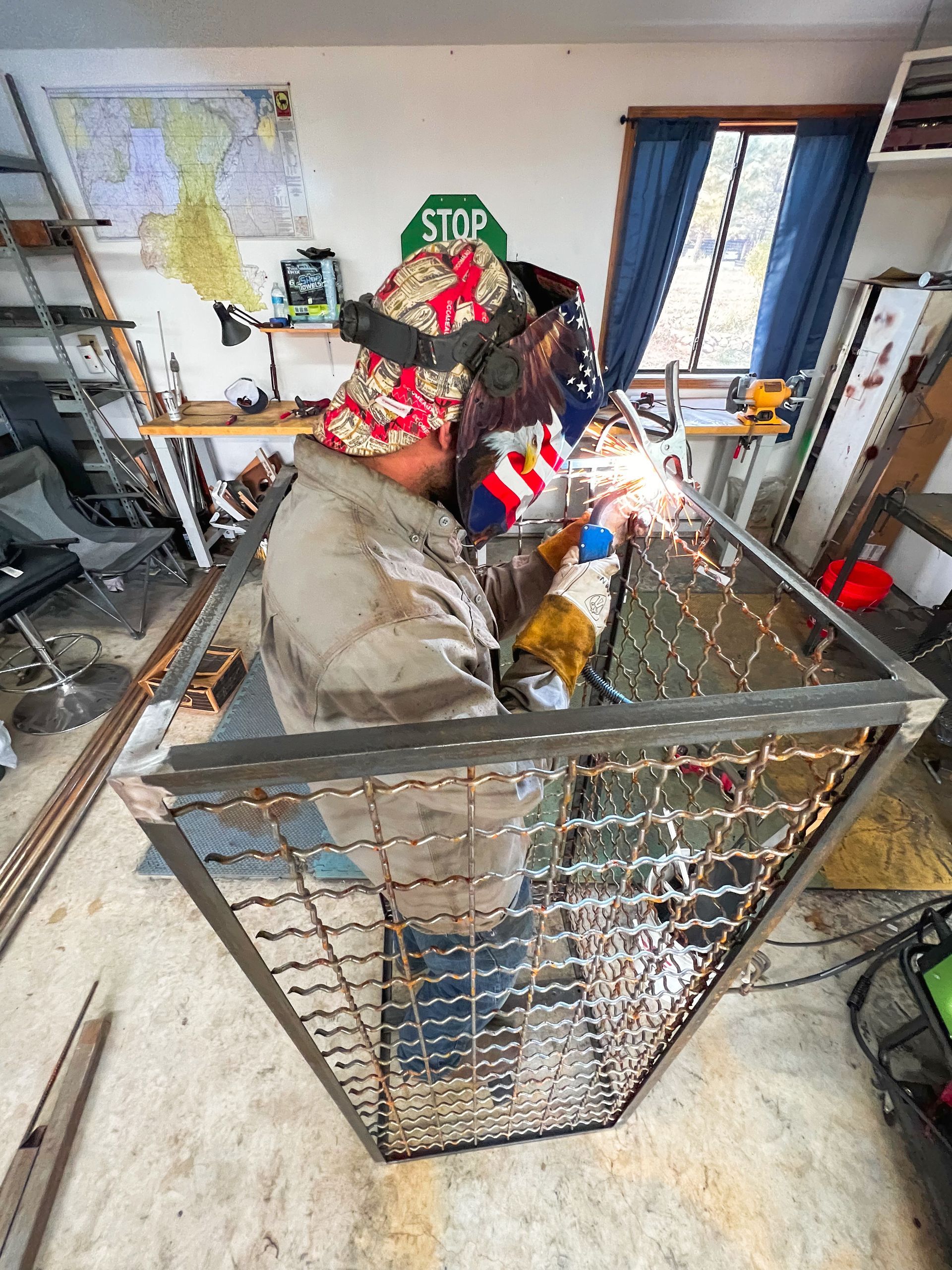 A man is welding a piece of metal in a room with a stop sign in the background.