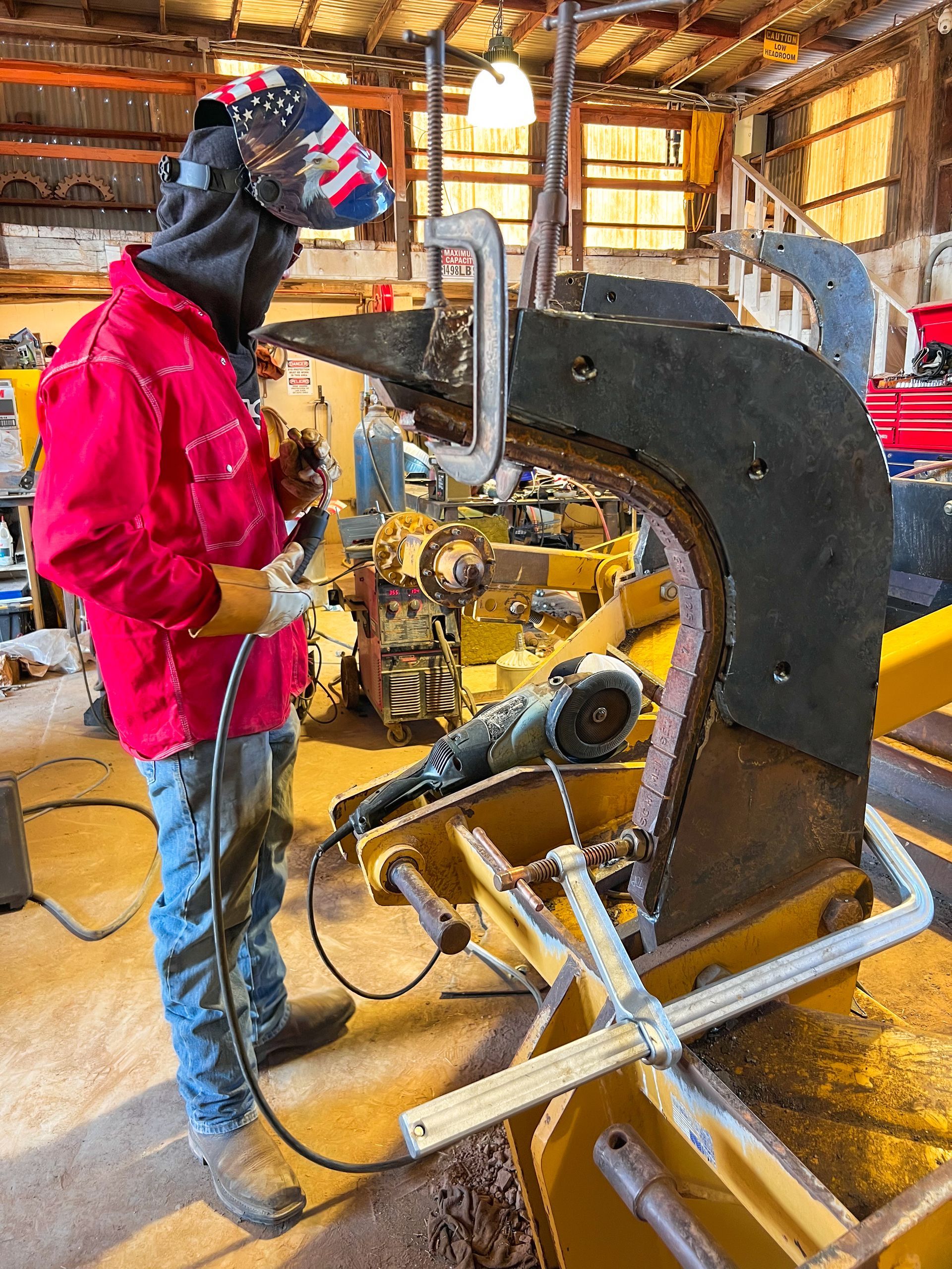 A man wearing a welding mask is working on a piece of metal.