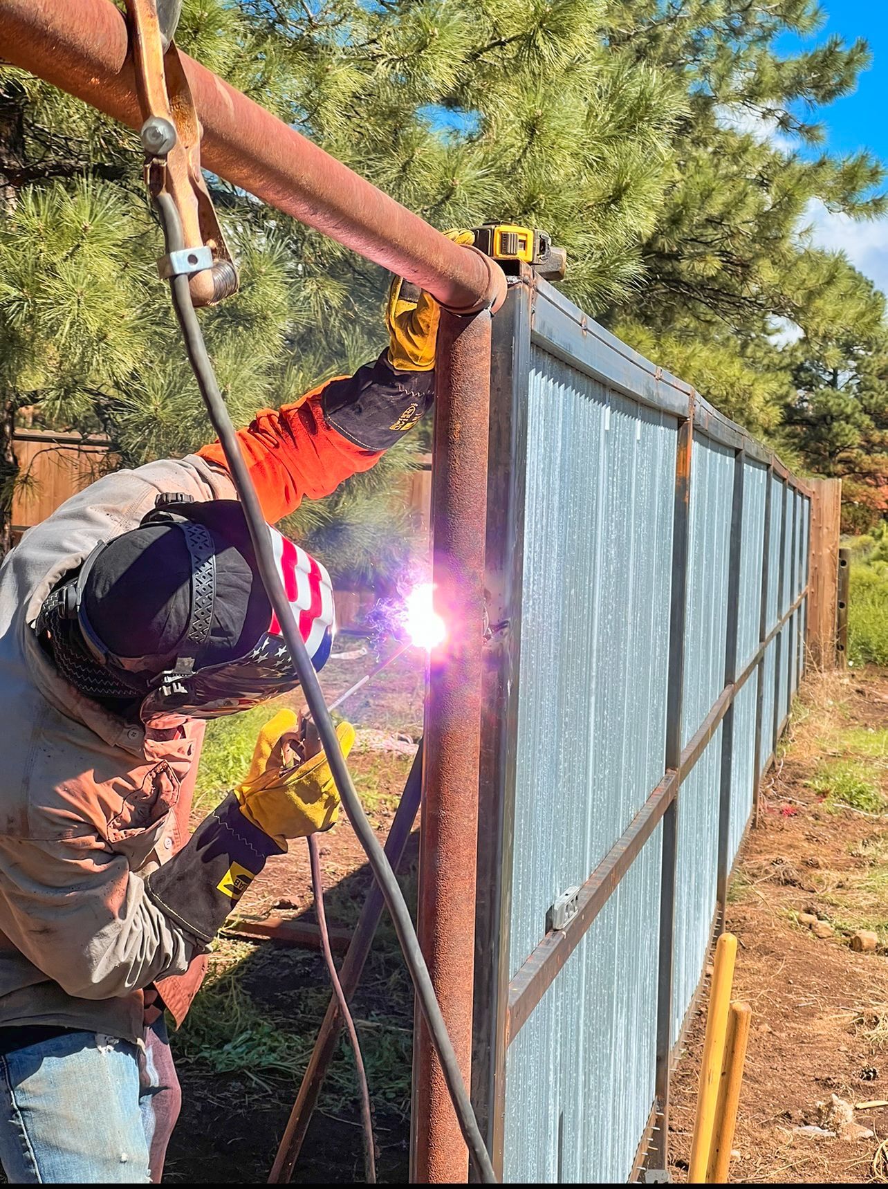 A man is welding a metal fence in a field.