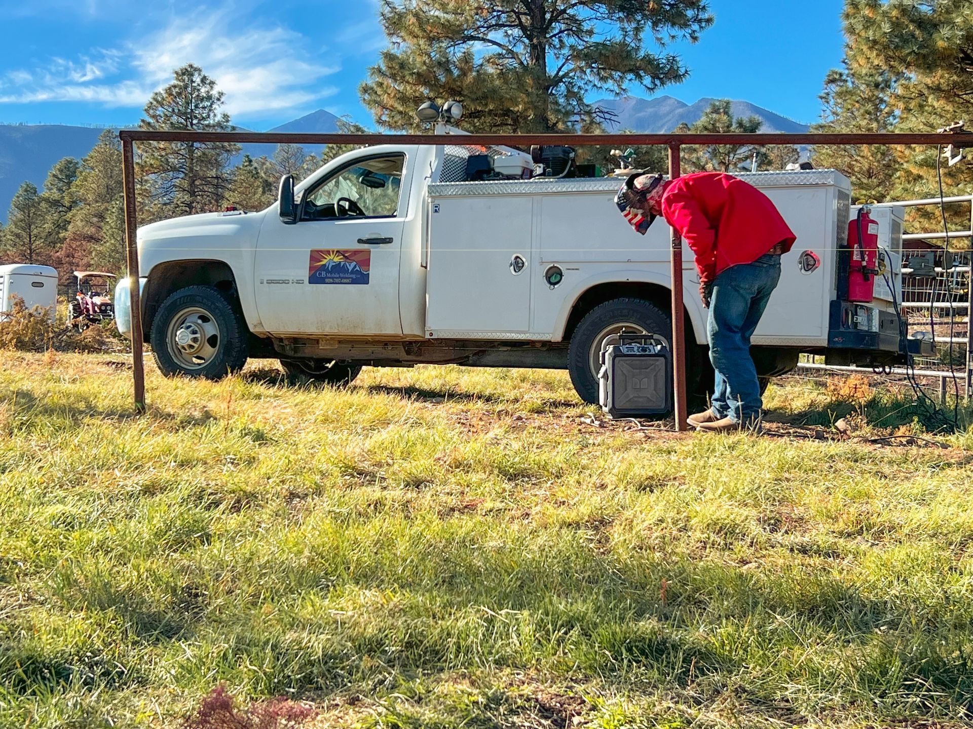 A man in a red jacket is leaning on a white truck in a grassy field.