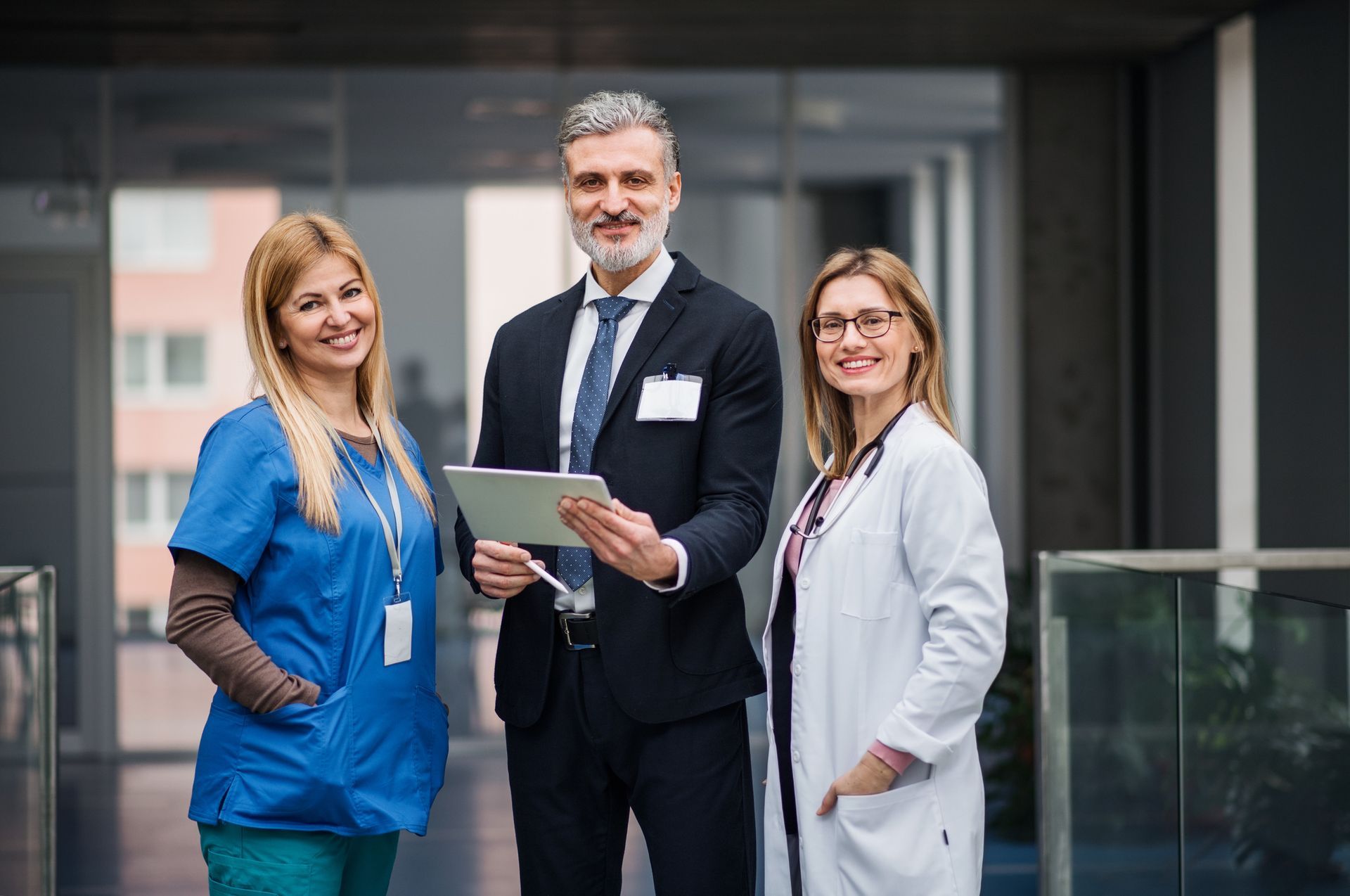 Three professionals standing in a modern office, one holding a tablet and two wearing badges and lanyards.