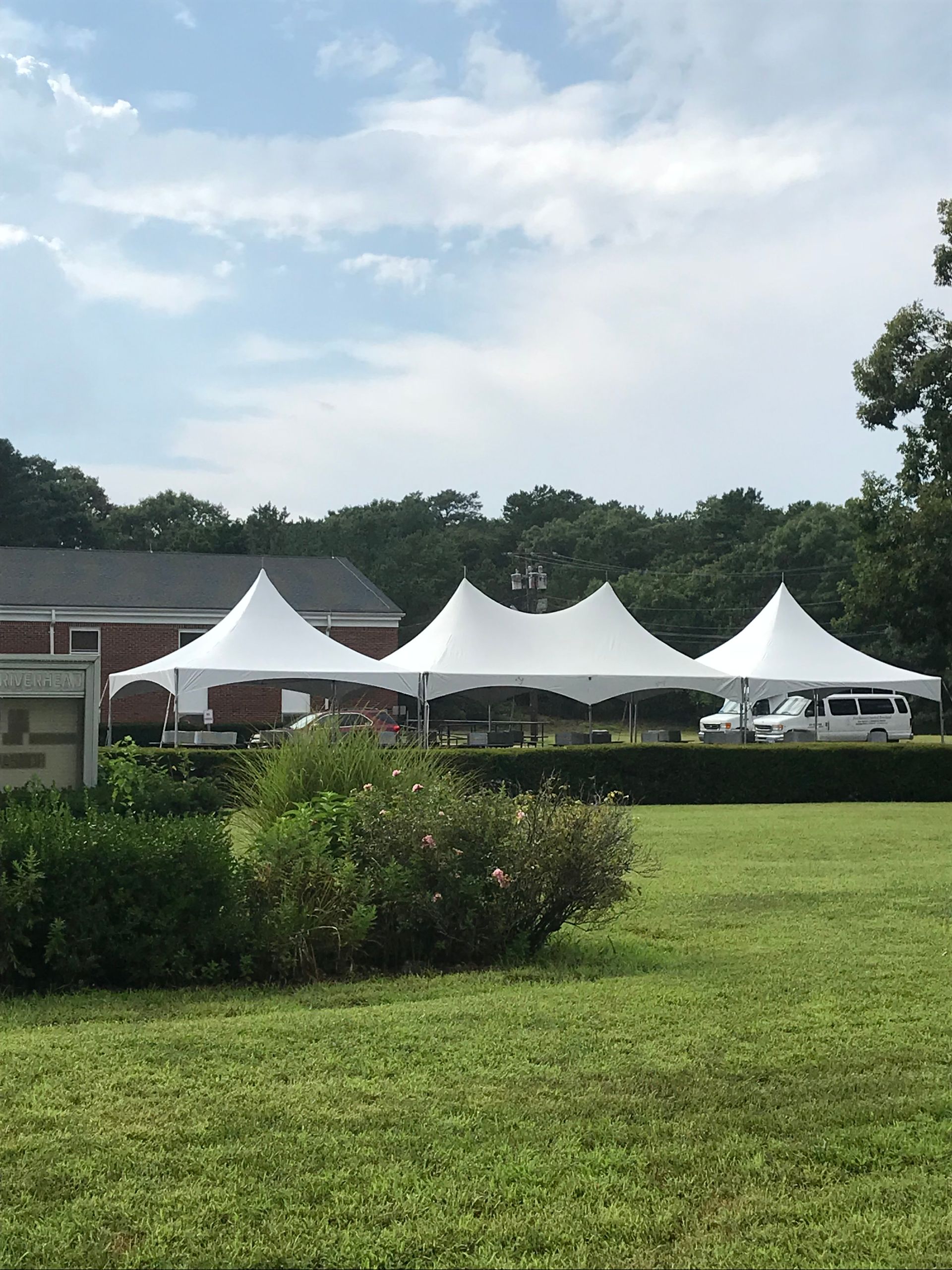 A row of white tents are set up in a grassy field