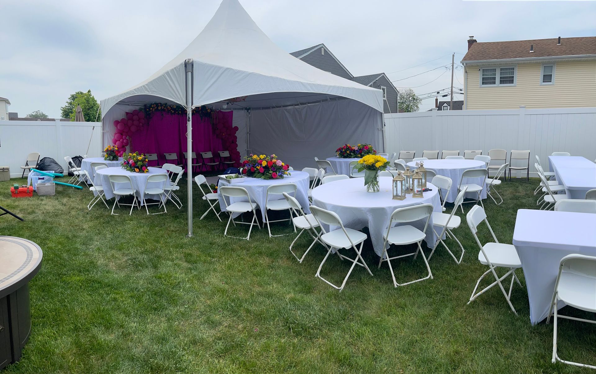 Tables and chairs are set up in a backyard under a tent.