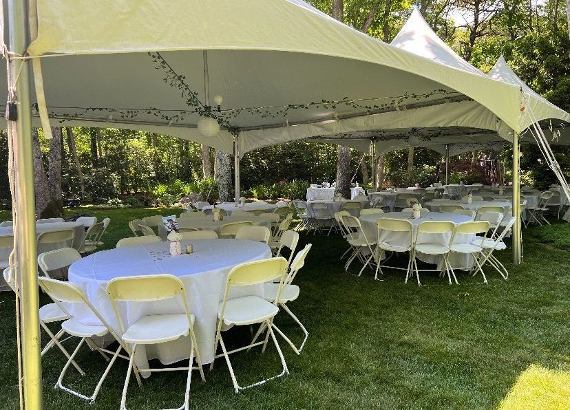 Tables and chairs are set up under a tent in the grass.