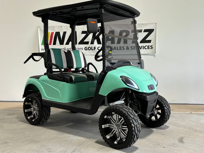 Green golf cart with black roof and wheels, parked in front of a banner.