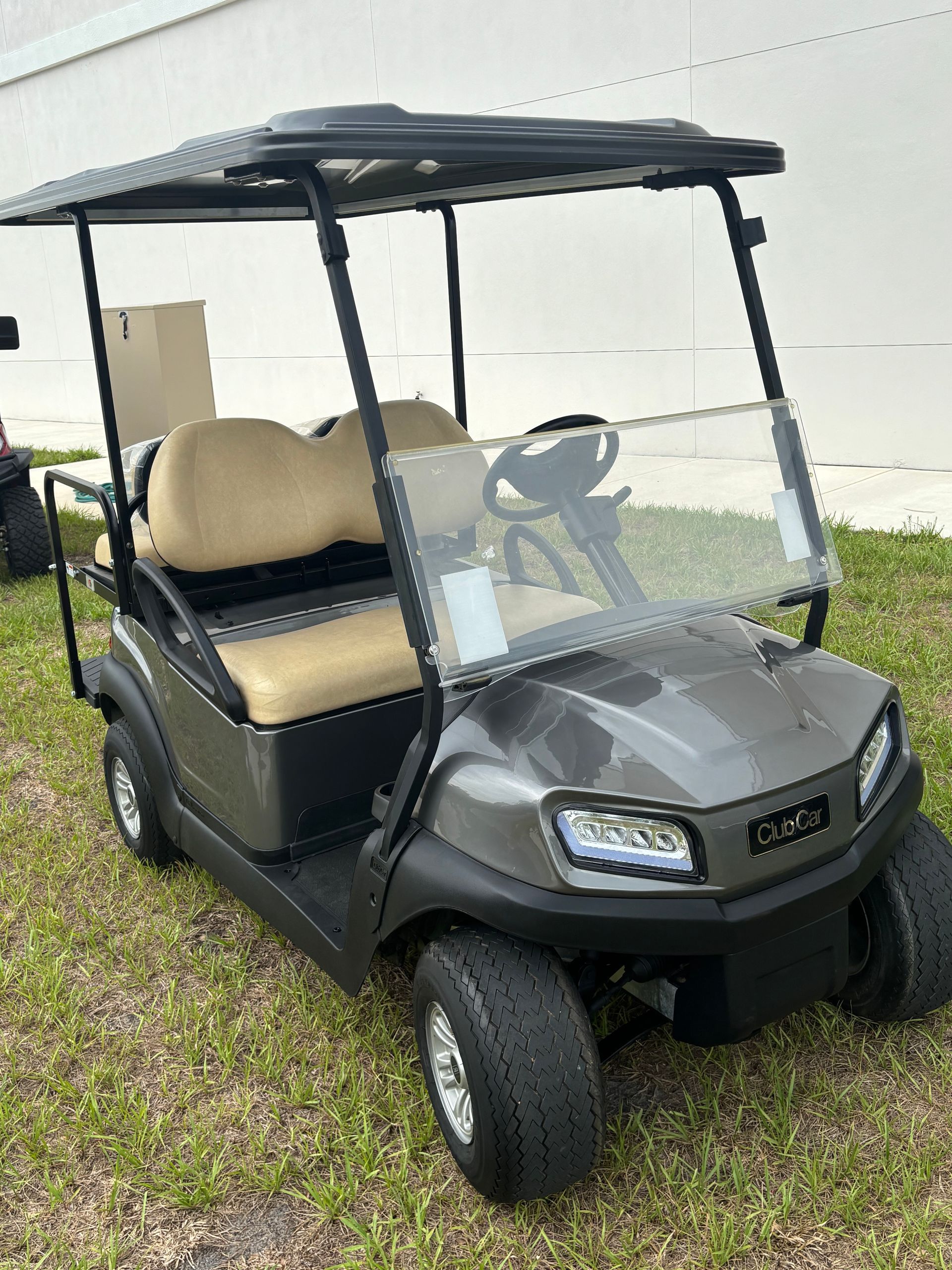Gray golf cart with tan seats and a black roof, parked on grass.