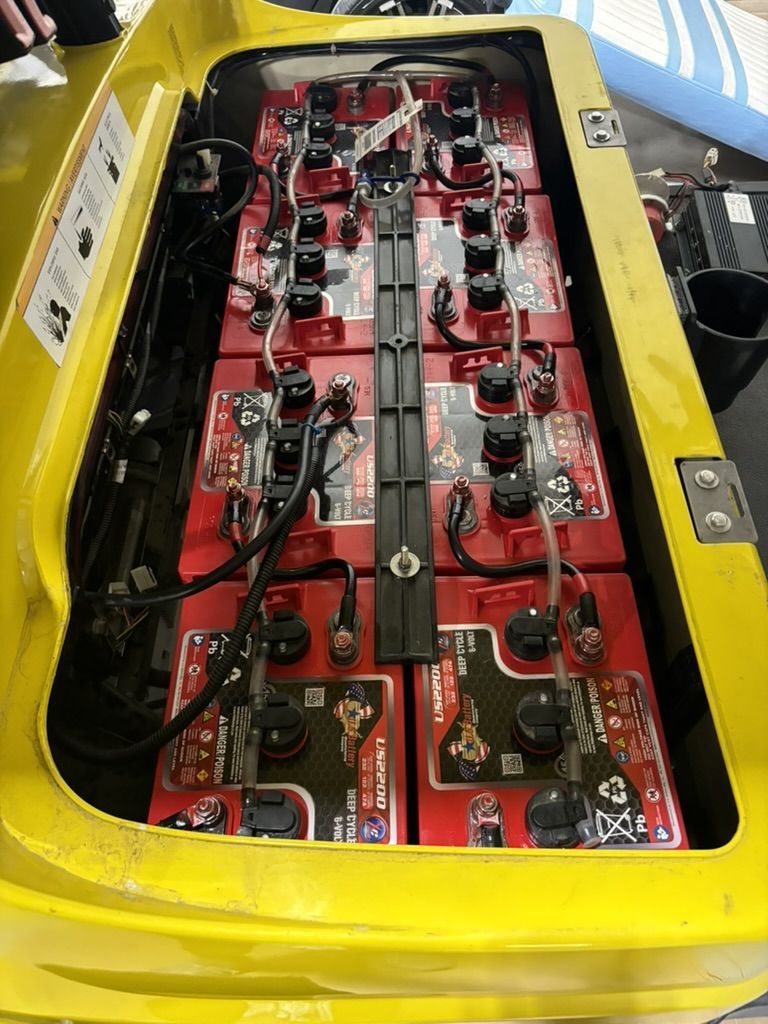 Yellow vehicle battery compartment with red batteries and black wiring.