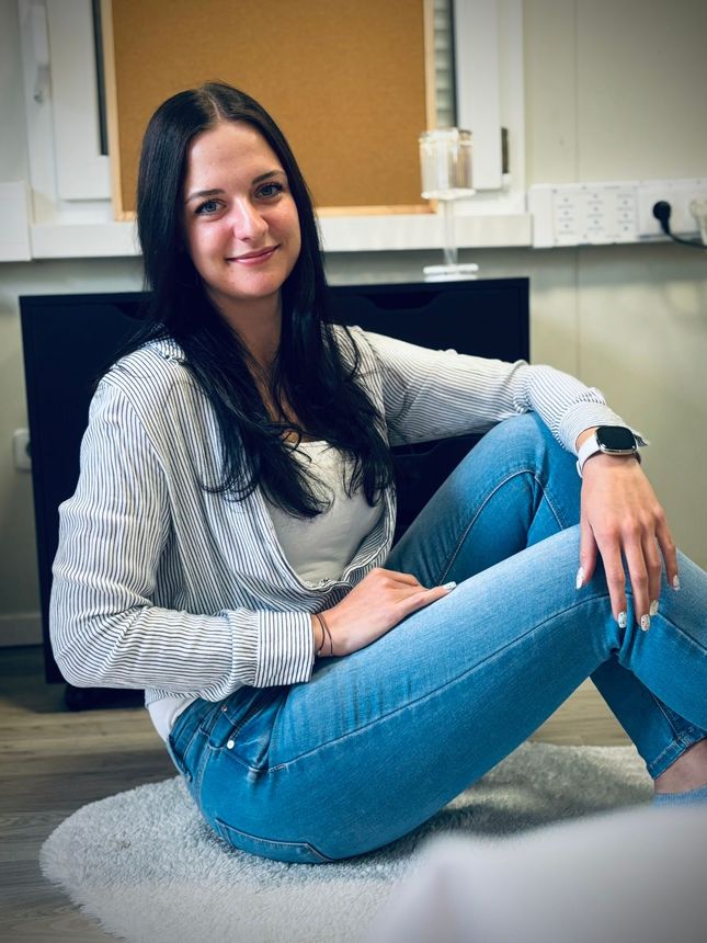 Eine Frau sitzt in Jeans und mit einer Uhr auf dem Boden.