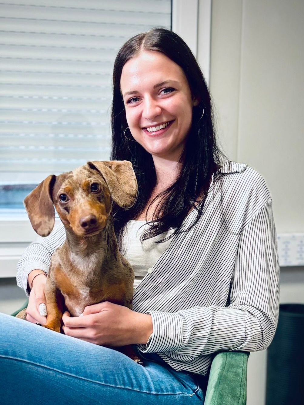 Eine Frau sitzt auf einem Stuhl und hält einen kleinen Hund.