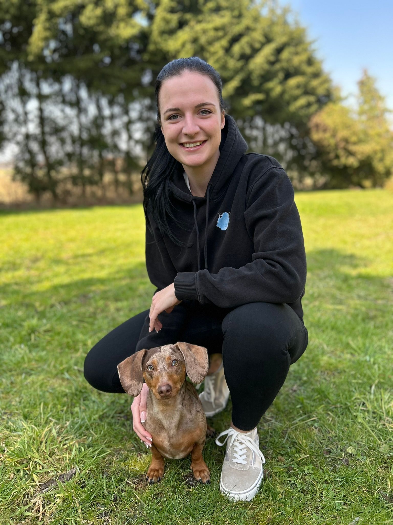 Eine Frau sitzt auf einem Stuhl und hält einen kleinen Hund.