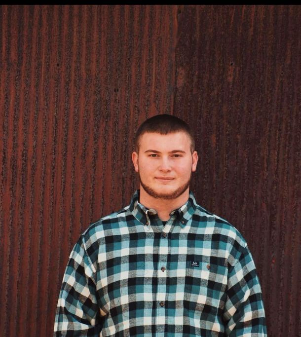 A man in a plaid shirt is standing in front of a rusty wall