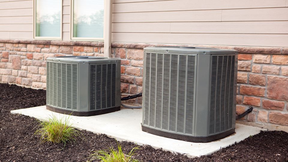 Two air conditioners are sitting on the side of a house.