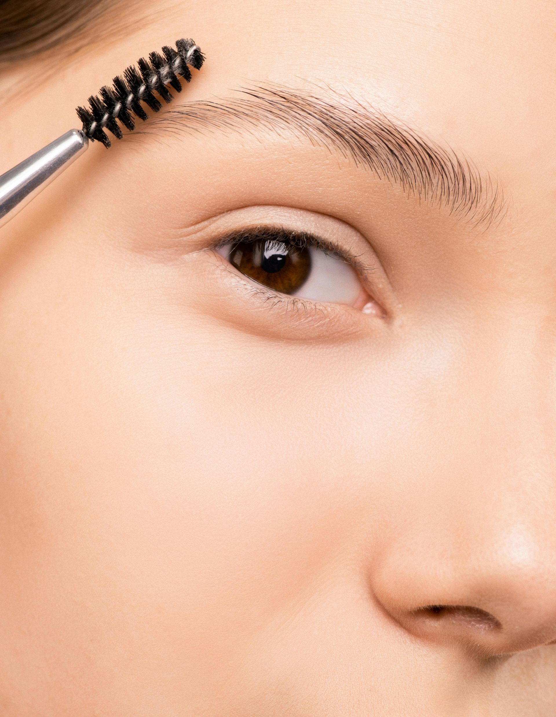 A woman is brushing her eyebrows with a brush.