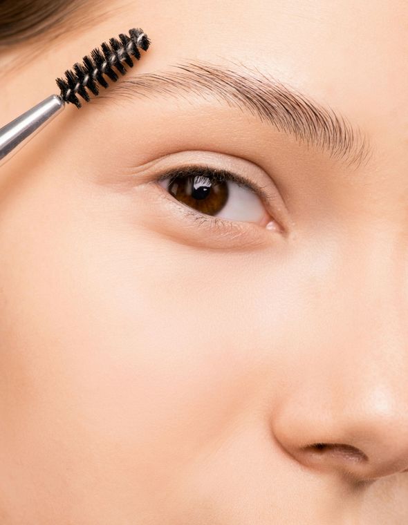 A woman is brushing her eyebrows with a brush.