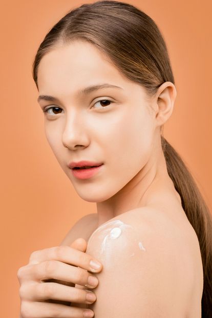 A woman is applying lotion to her shoulder.