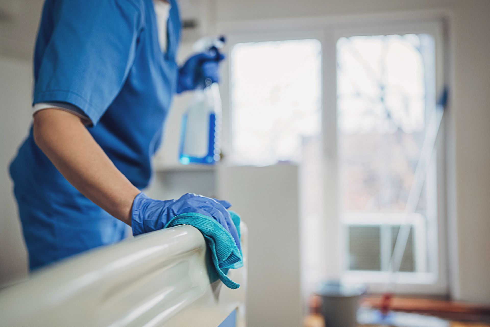 Un'infermiera sta pulendo un letto d'ospedale con un panno e uno spruzzino.