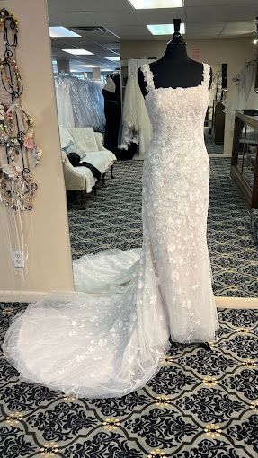 A white wedding dress is on a mannequin in a bridal shop.