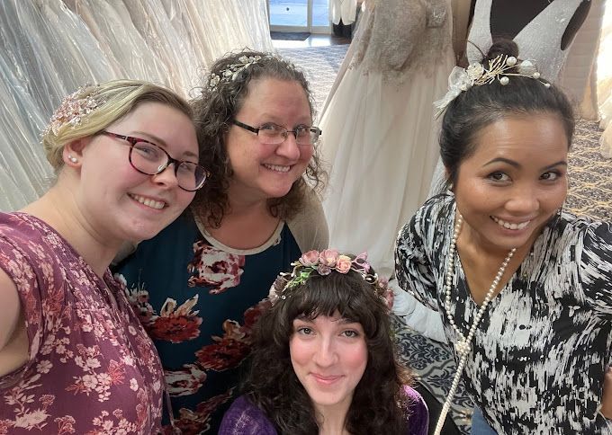 A group of women are posing for a picture in front of a wedding dress.
