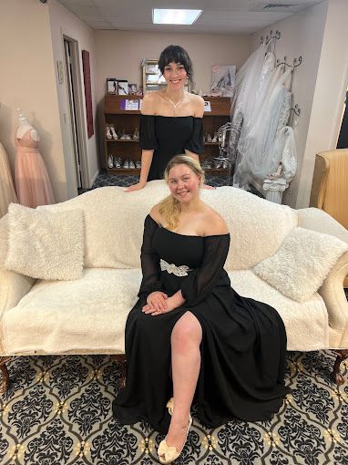 Two women in black dresses are sitting on a white couch.