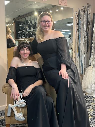 Two women in black dresses are sitting next to each other in a chair.