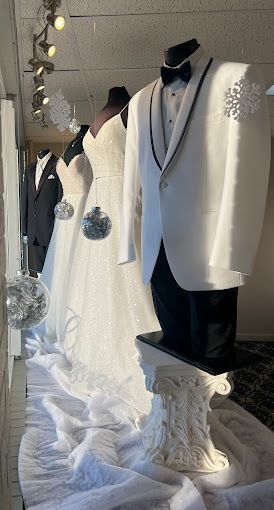 A row of wedding dresses and tuxedos on mannequins in a store window.
