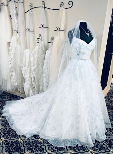 A white wedding dress with a veil is on a mannequin in a bridal shop.