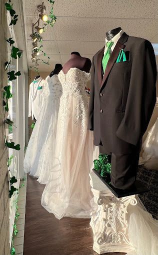 A row of wedding dresses and a groom 's suit are on display in a store.