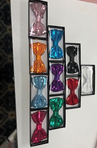 There are many different colored bow ties in boxes on the wall.