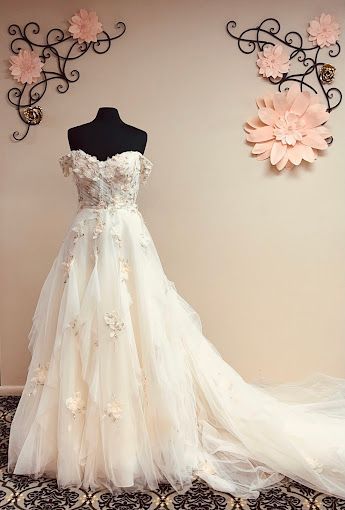 A wedding dress is on a mannequin in front of a wall with paper flowers.