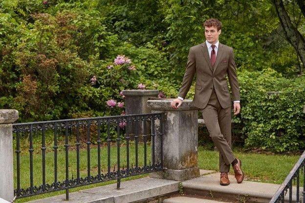 A man in a suit and tie is leaning against a railing in a park - Salina, KS - Princess & Penguin Formalwear