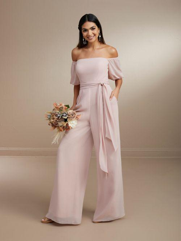 A woman is wearing a pink off the shoulder jumpsuit and holding a bouquet of flowers - Salina, KS - Princess & Penguin Formalwear