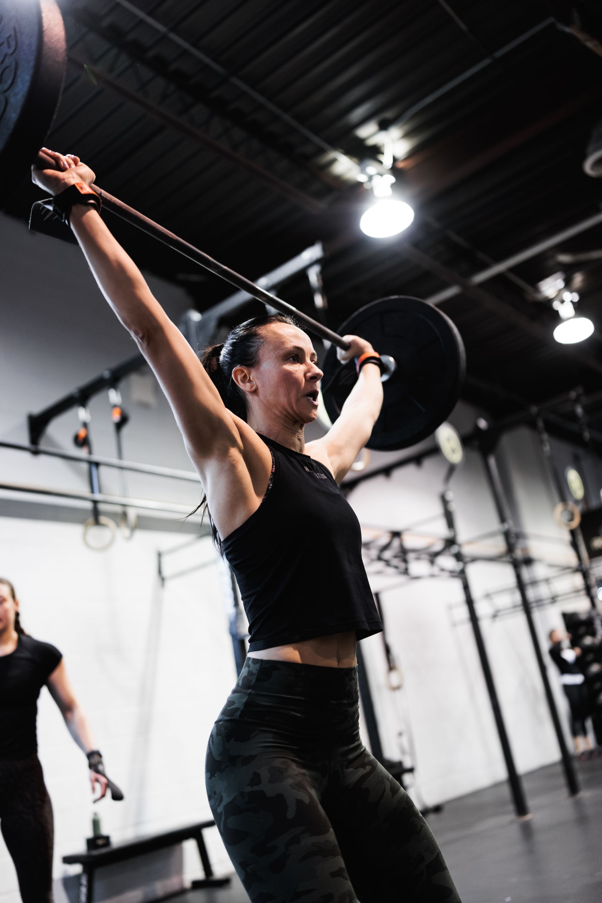 Woman lifting barbell overhead in gym.