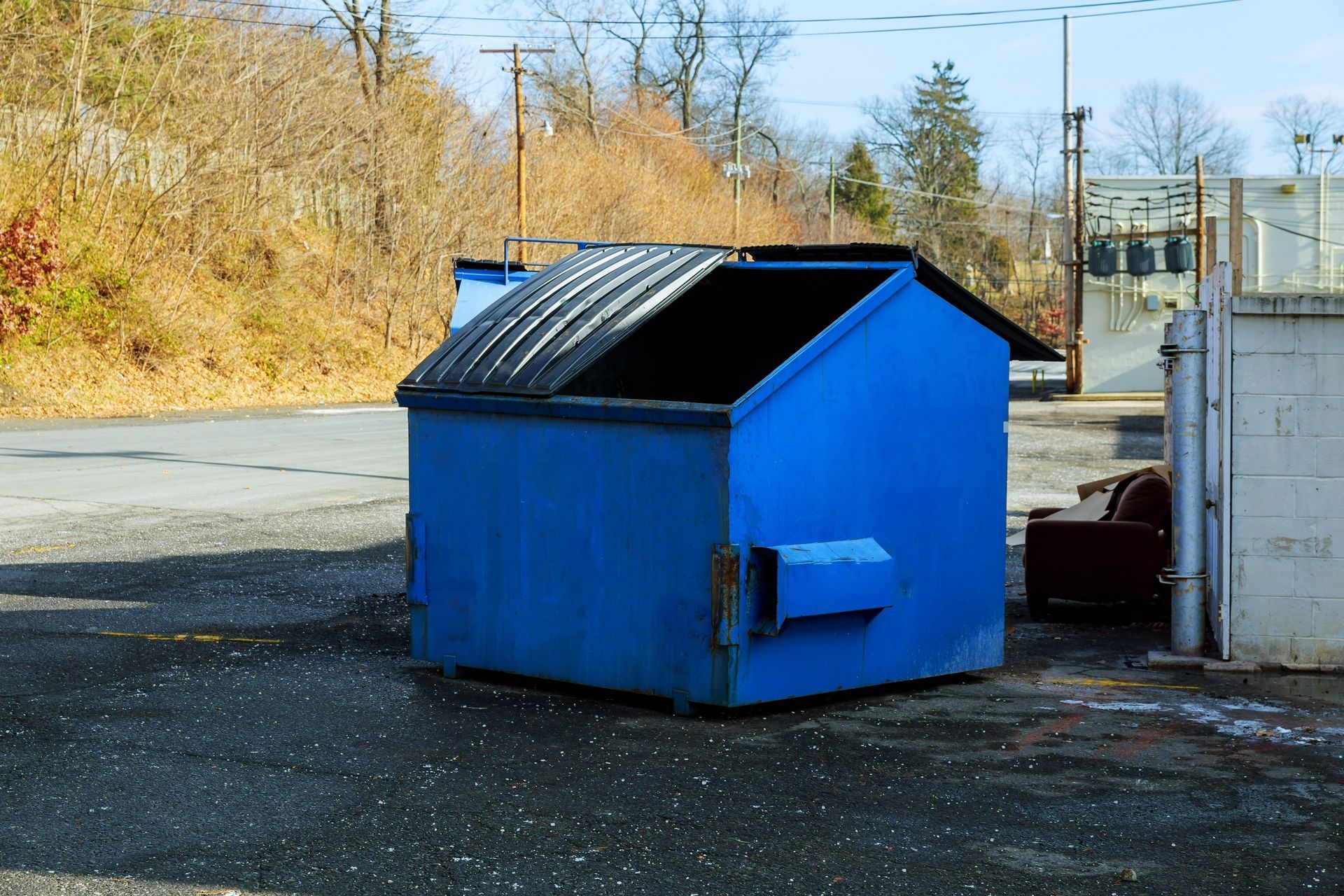 A blue dumpster is sitting in the middle of a parking lot.