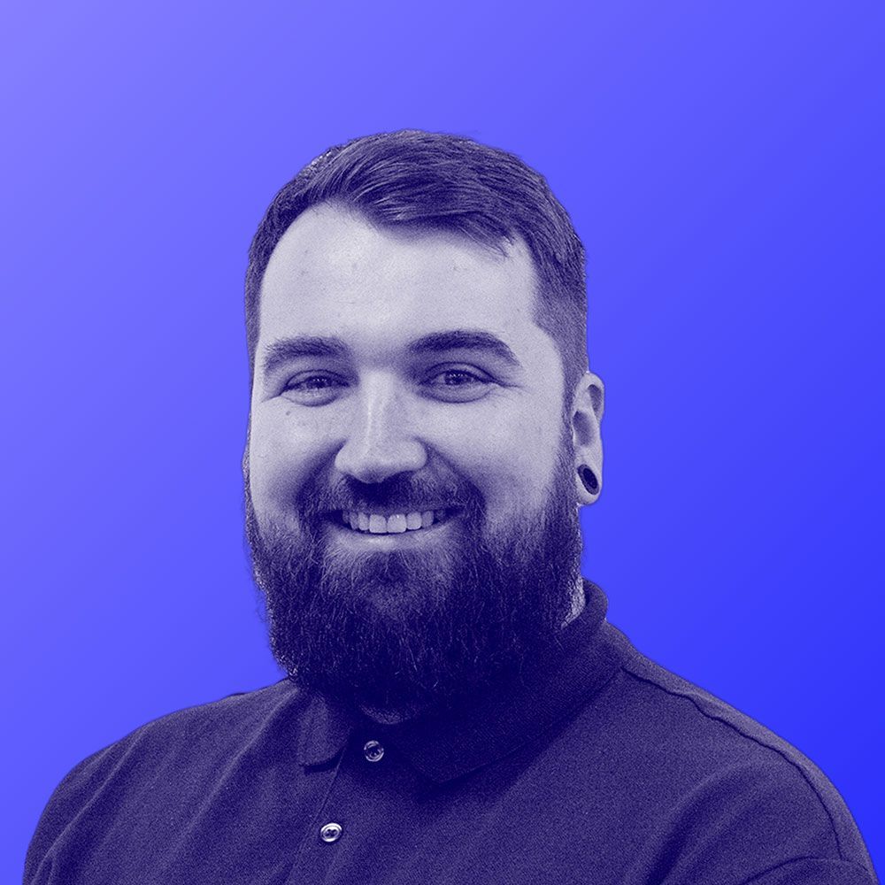 A man with a beard is smiling in front of a blue background.