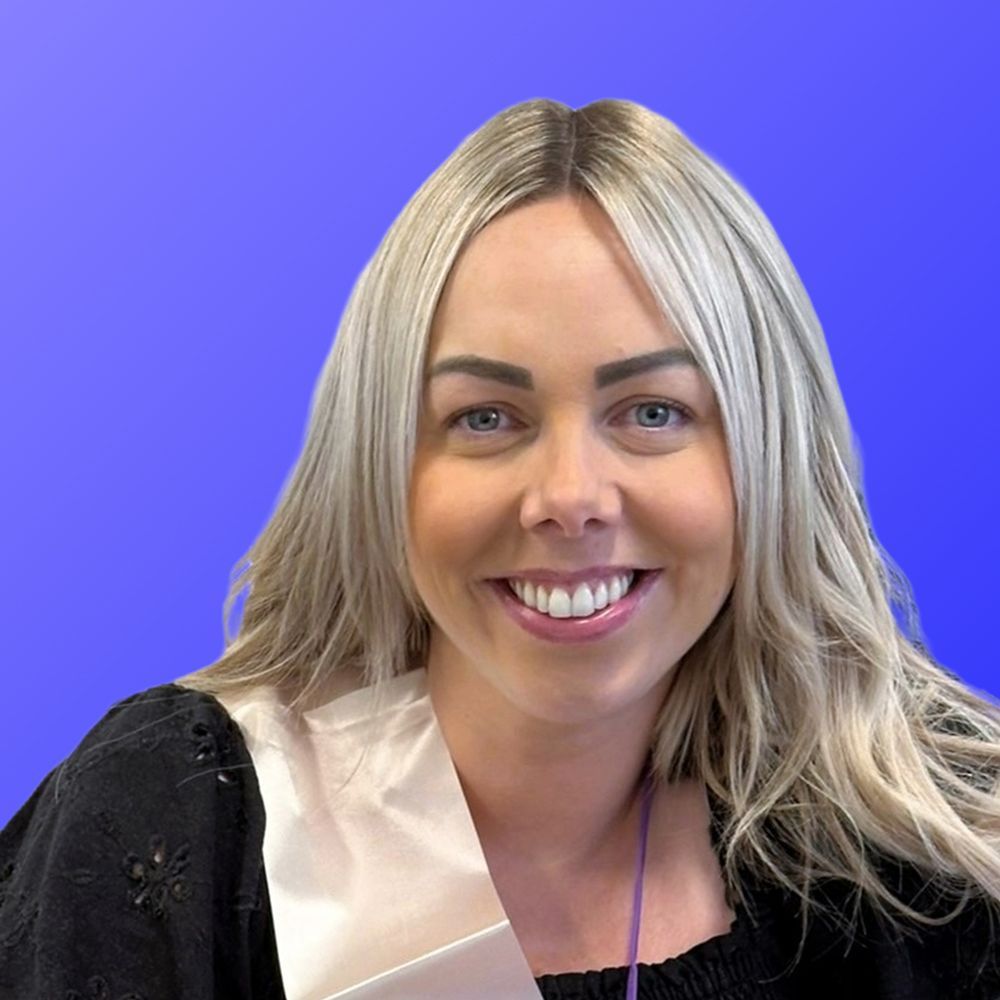 A woman in a paisley shirt is smiling in front of a blue background.