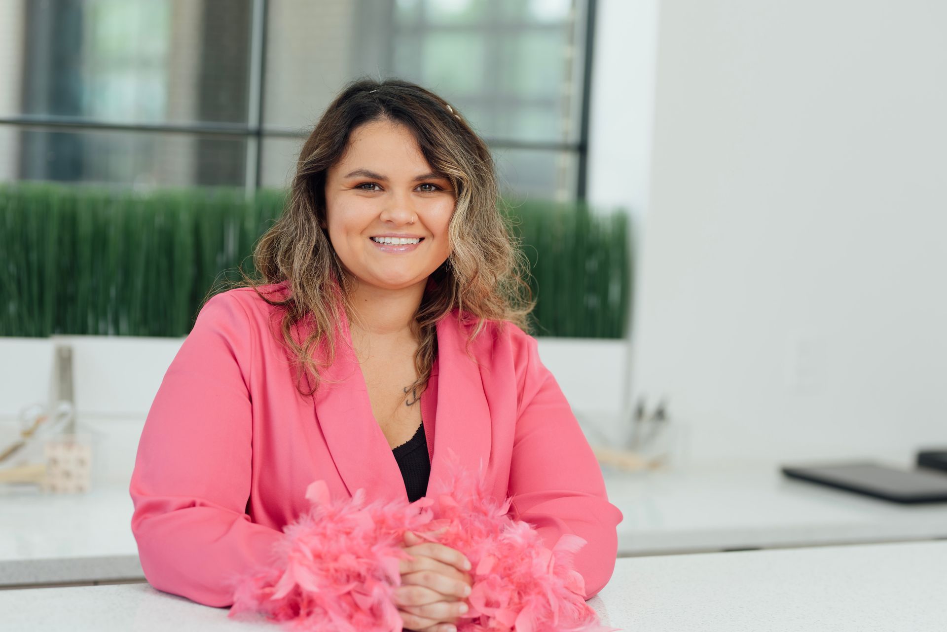 A woman in a pink jacket is sitting at a table with a pink boa around her neck.