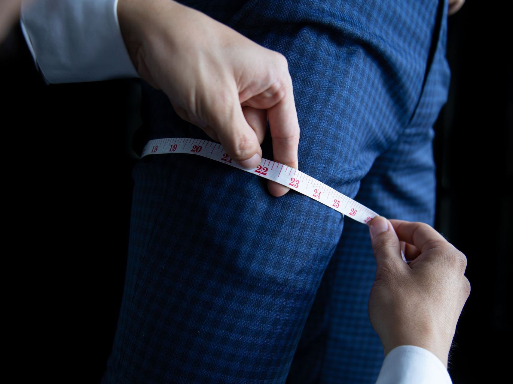A person is measuring a person 's pants with a tape measure.