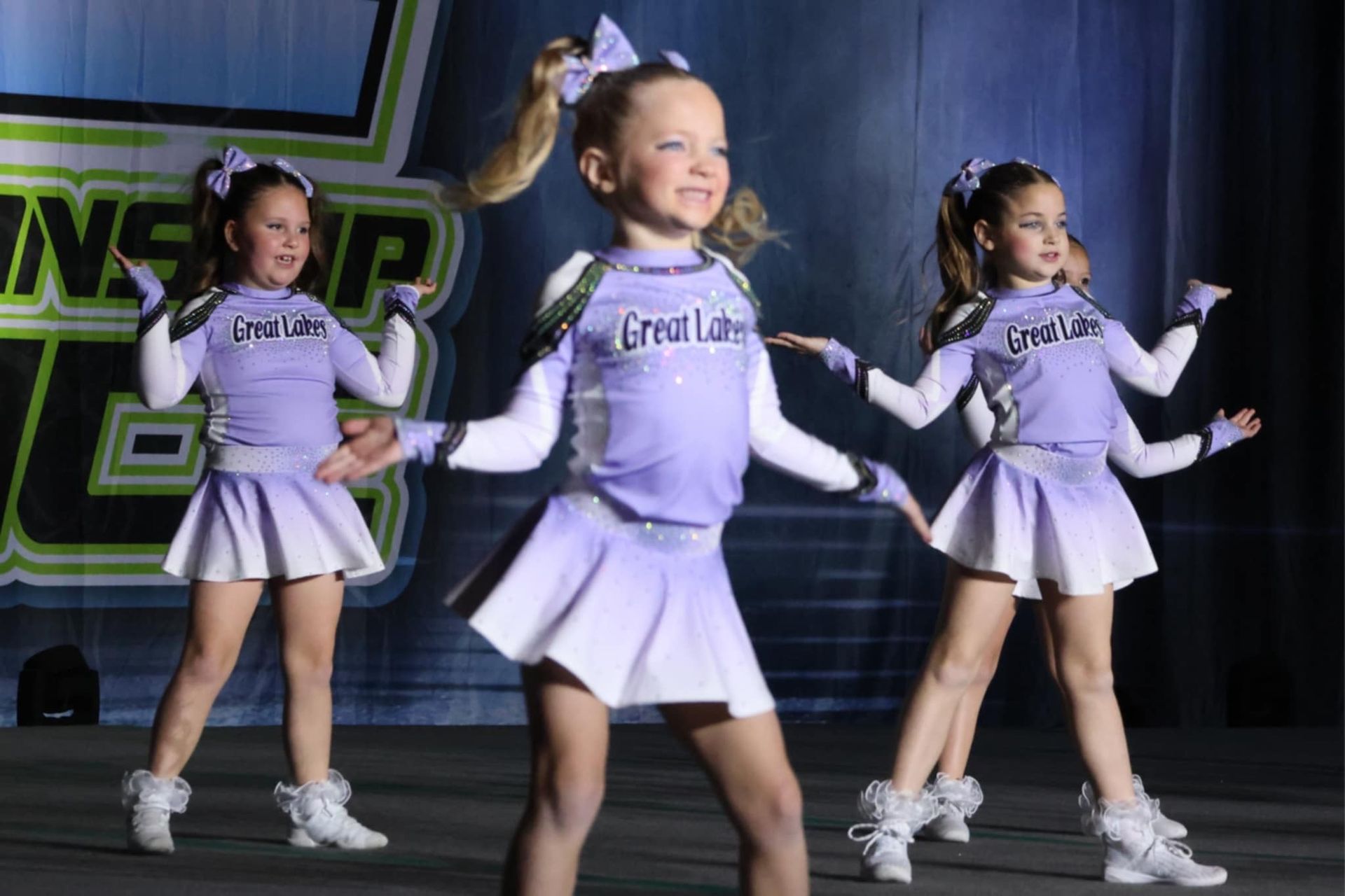 Three young girls in purple and white uniforms are dancing on a stage.