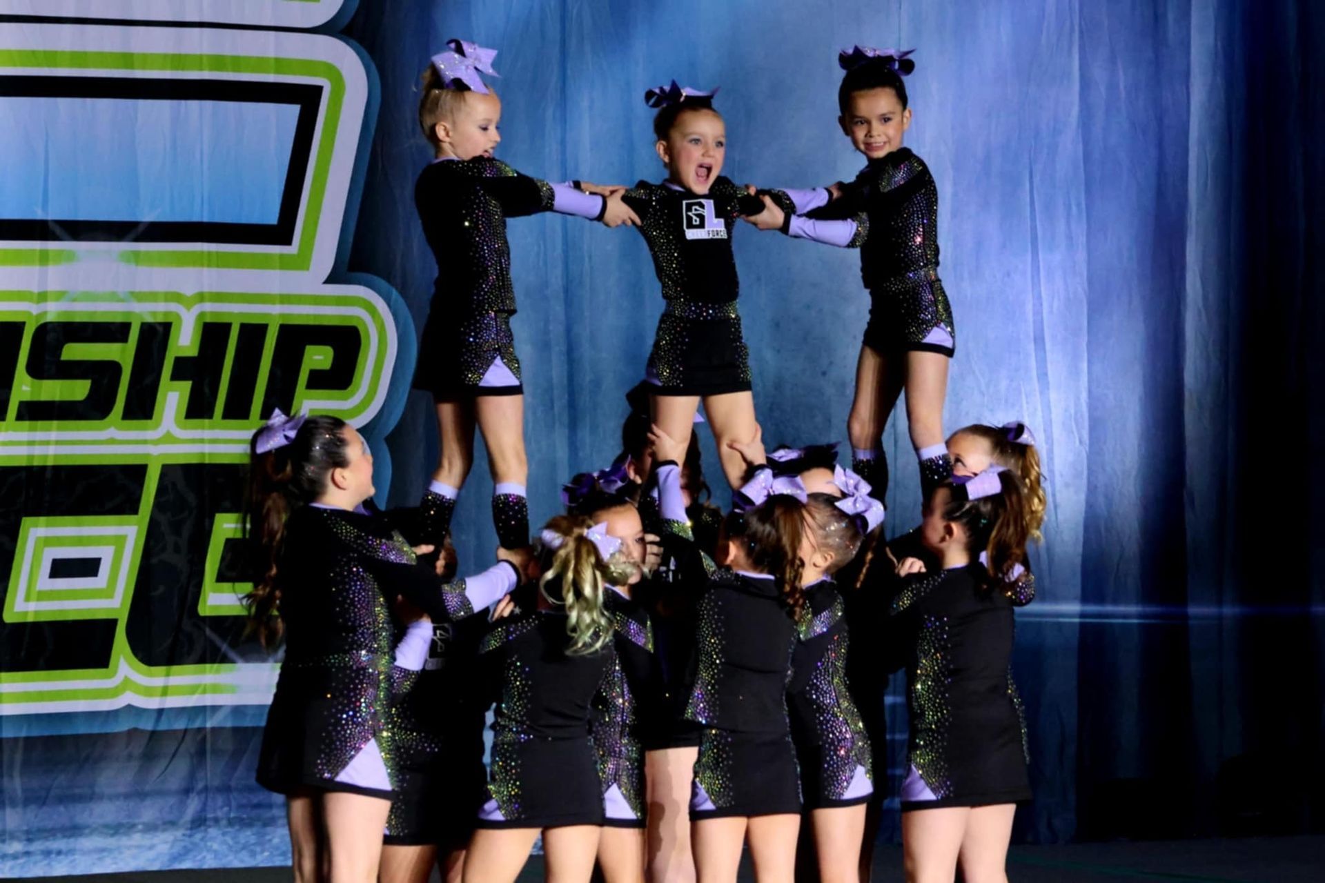 A group of cheerleaders are doing a pyramid on stage.