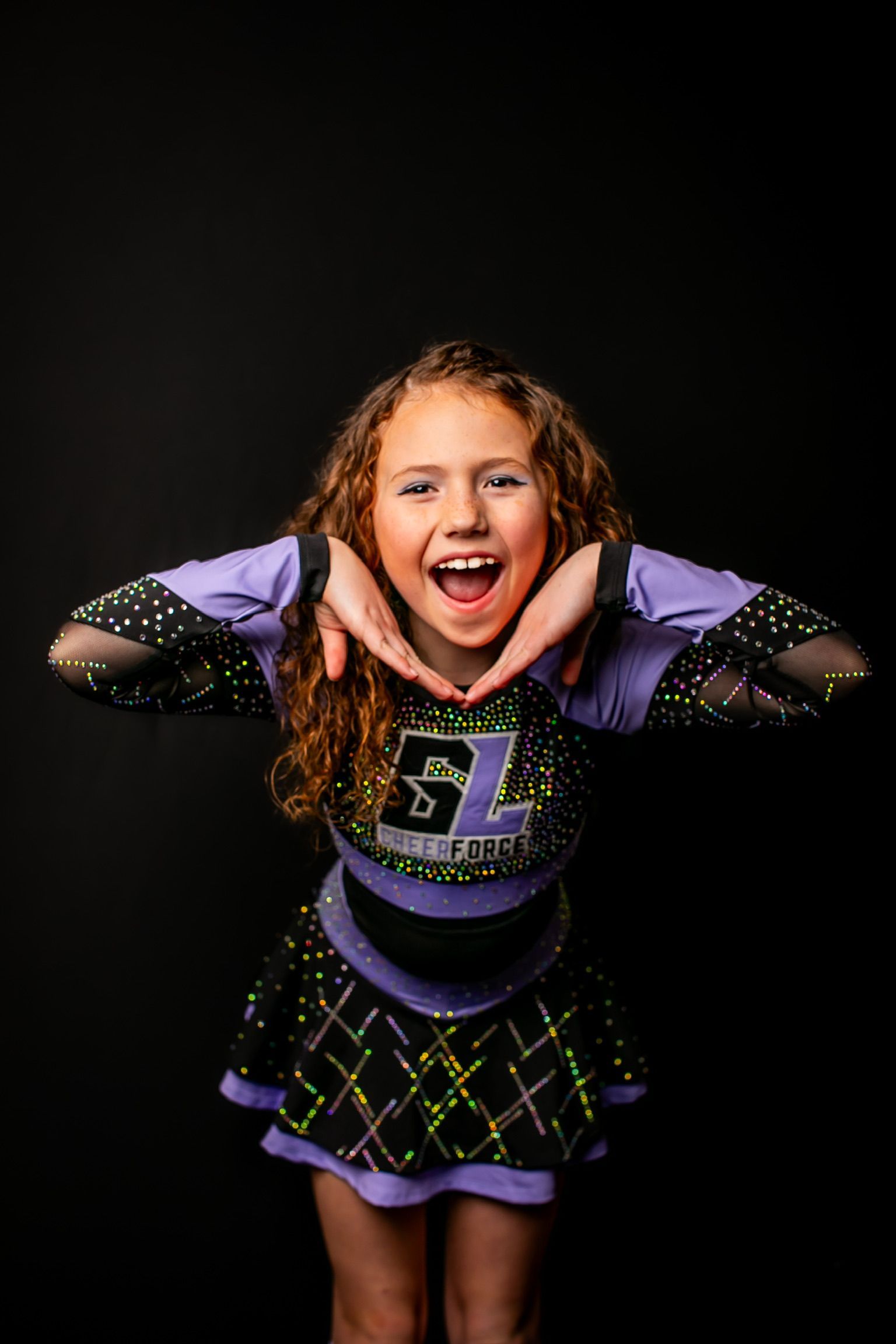 A young girl in a cheerleading uniform is making a heart shape with her hands.