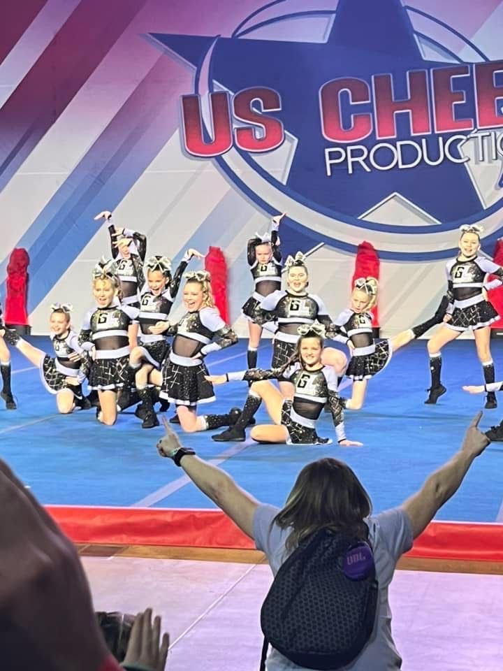 A group of cheerleaders are performing on a stage in front of a sign that says us cheer productions.
