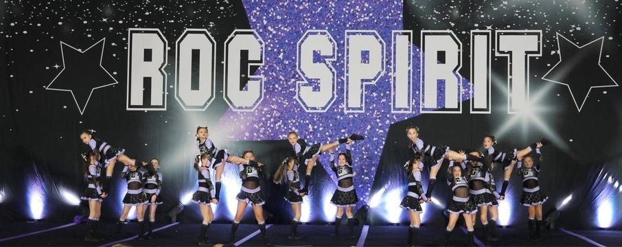 A group of cheerleaders are performing in front of a sign that says roc spirit