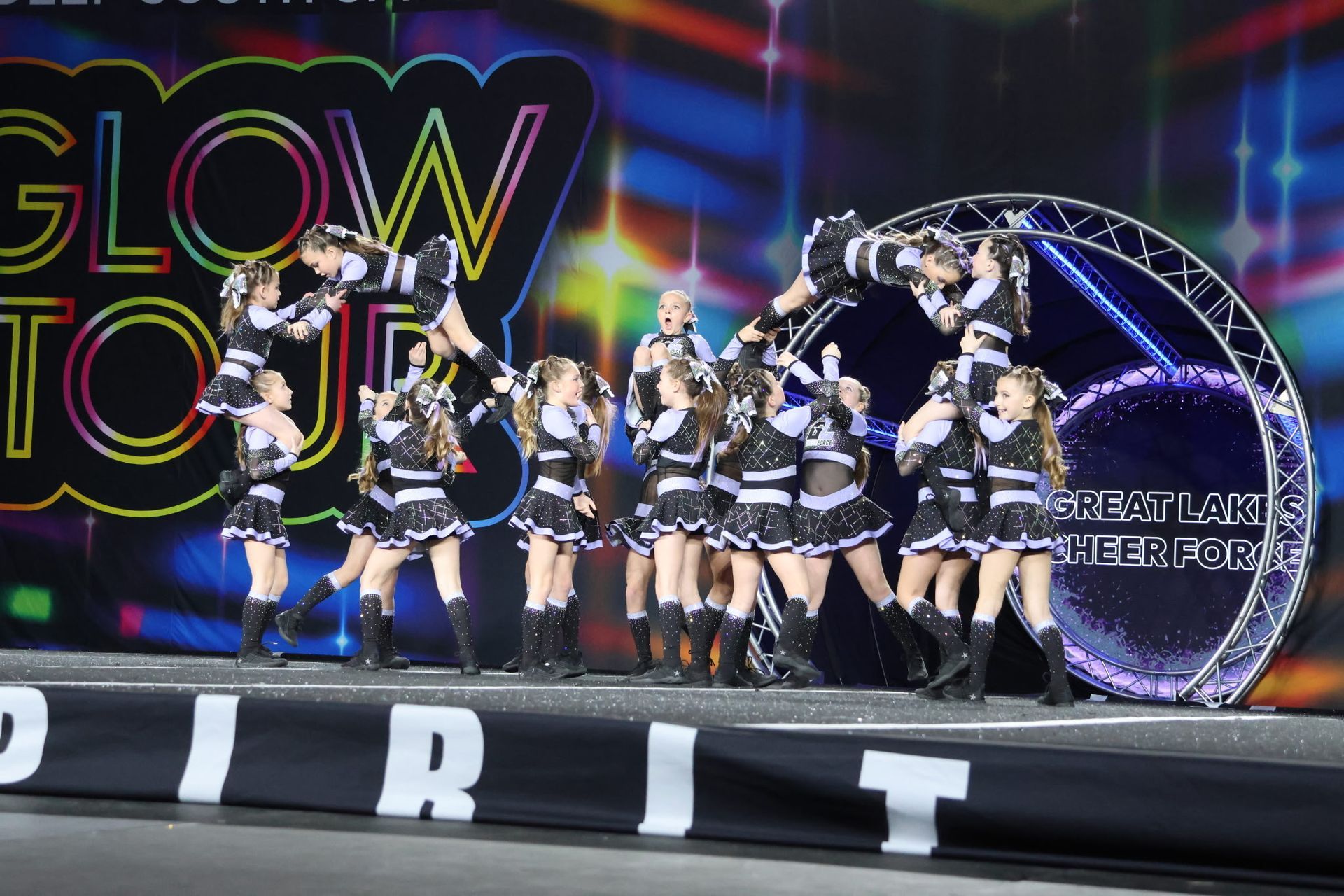 A group of cheerleaders are performing in front of a sign that says glow to the spirit