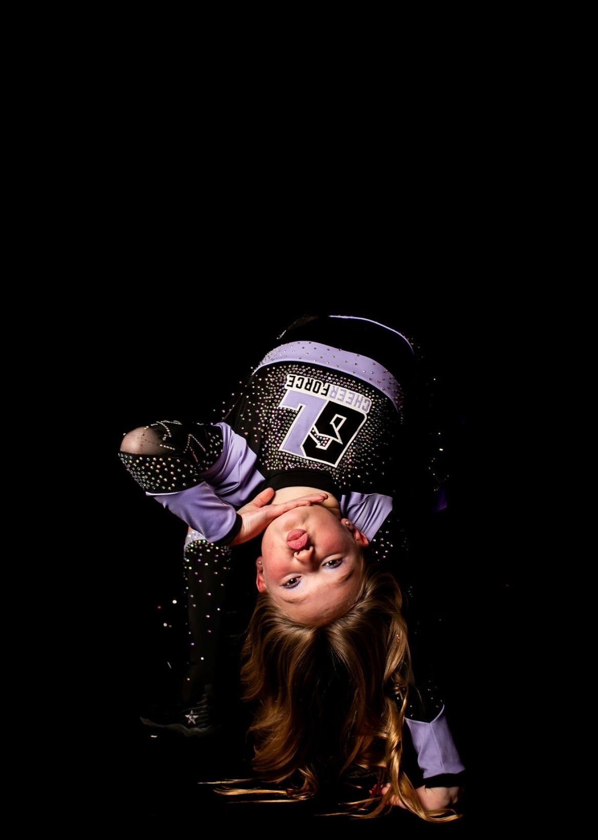 A young girl is doing a handstand on a black background.