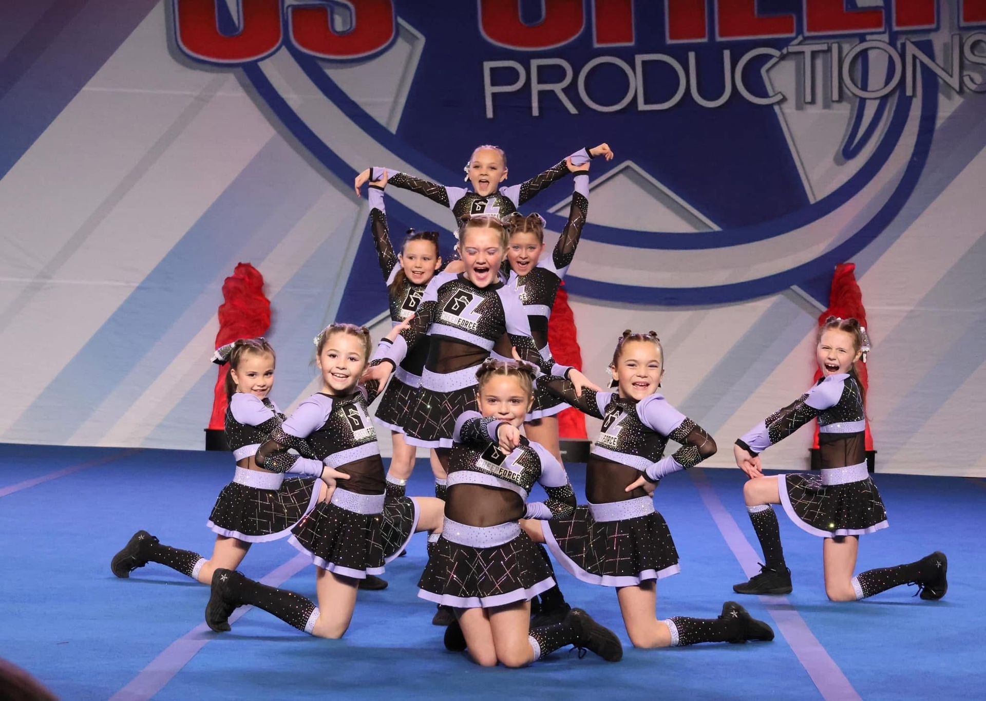 A group of cheerleaders are performing in front of a us cheer productions logo